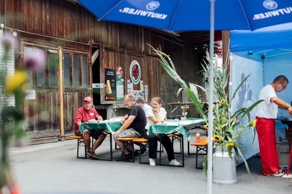 Guests sit at beer-table benches in front of the farm building.
