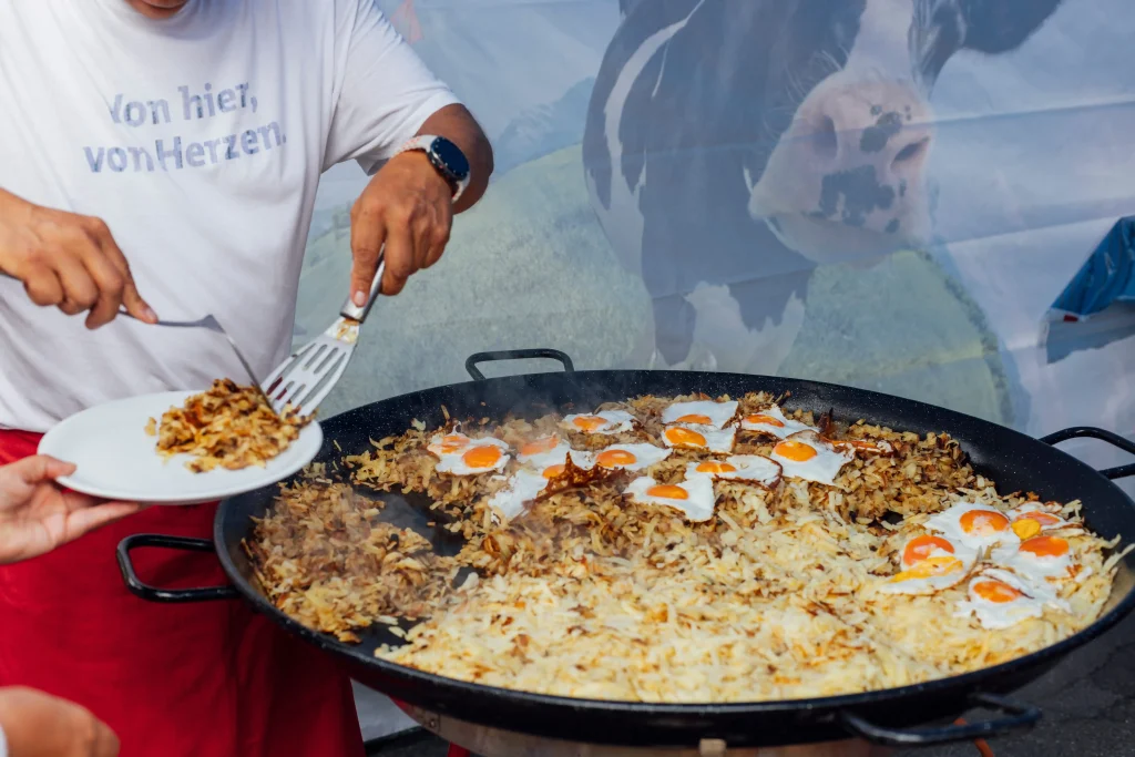 A person serves rösti and fried eggs from the pan.
