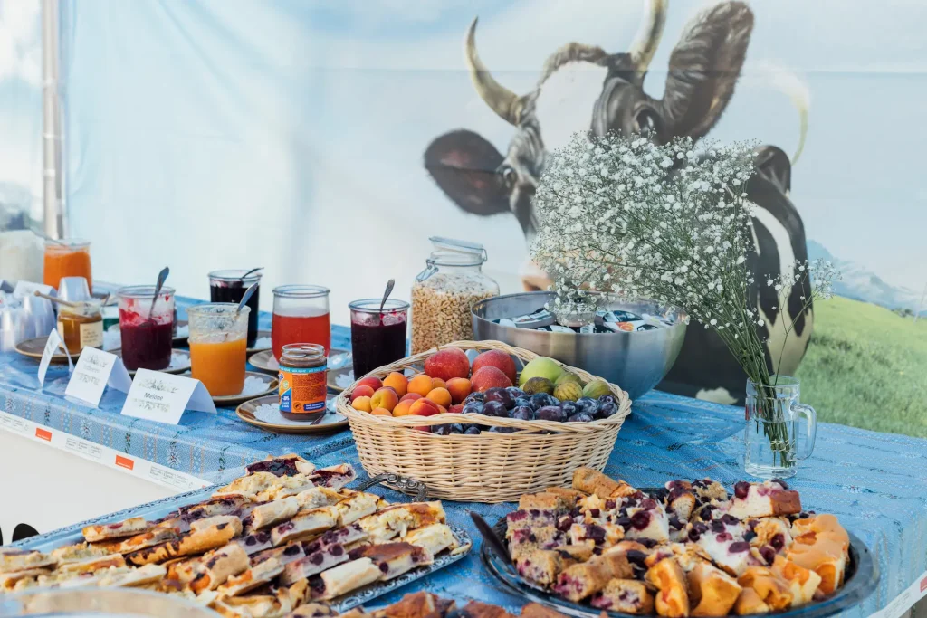 Breakfast buffet with jams, fruit juices, and croissants, with a cow poster in the background.