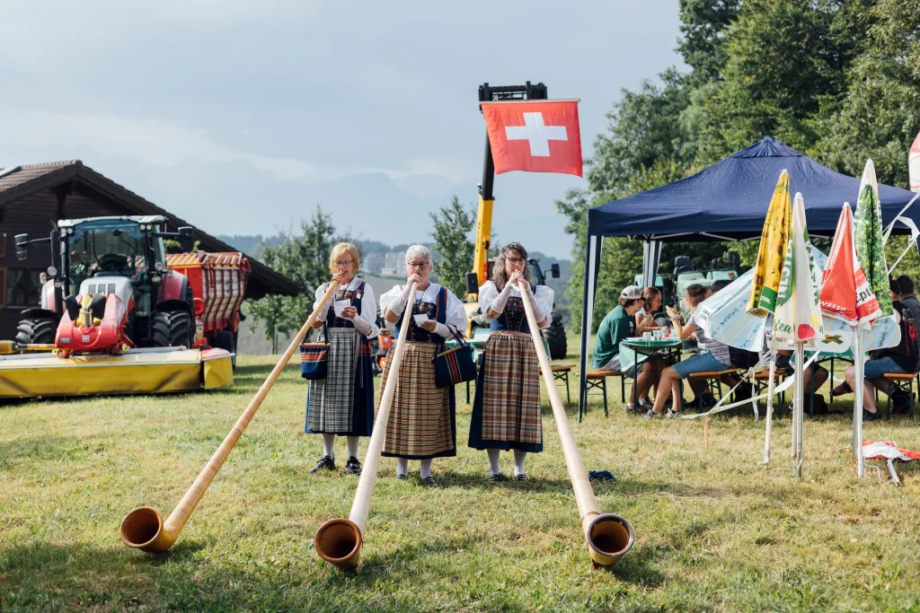 Women in traditional dress play alphorns in the festival meadow.