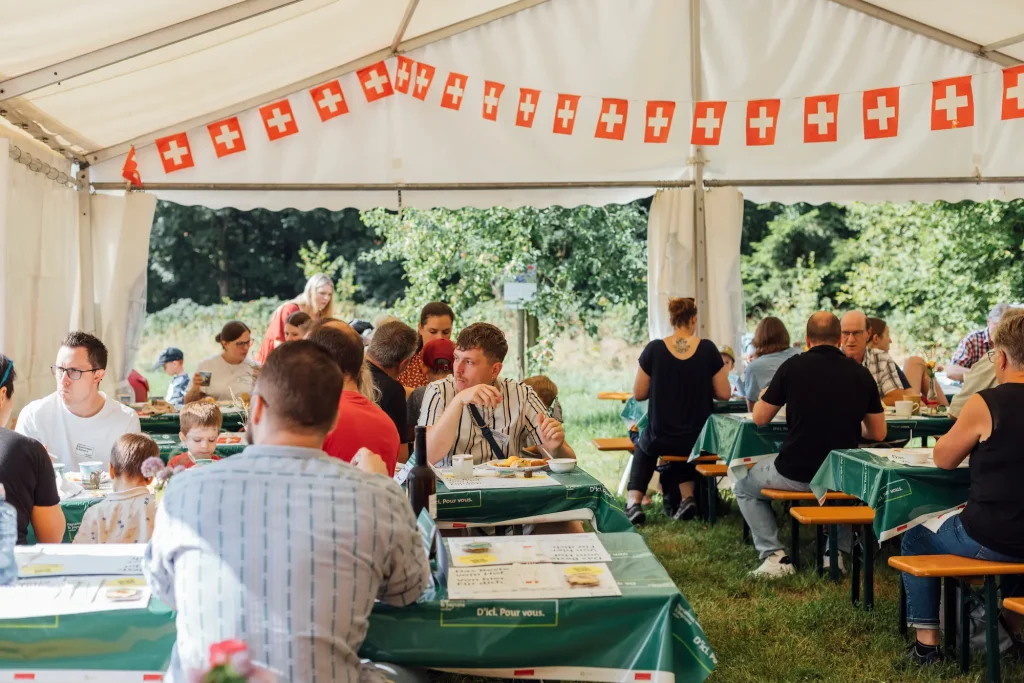 Visitors sit under the festival tent with a garland of Swiss flags.
